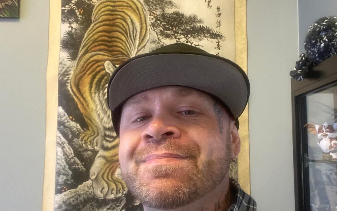 Man smiling in front of tiger artwork.
